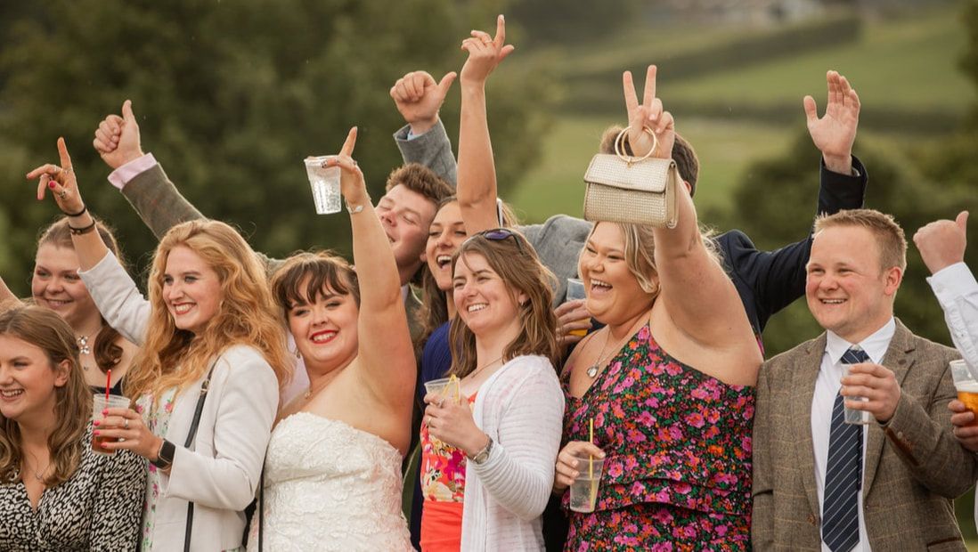 Wedding guests raise their glasses in celebration during an outdoor reception ceremony.