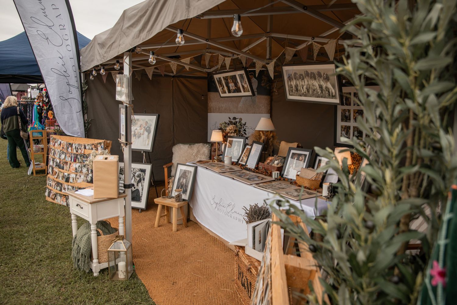 Rustic outdoor market stall with framed artwork, vintage decor, and string lights under a canvas tent.