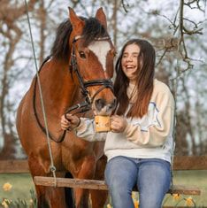 A beautiful chestnut horse stands next to someone in a cream sweater enjoying a sunny autumn day outdoors.