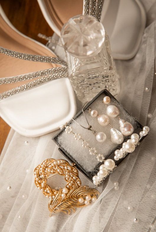 Elegant wedding accessories including pearl hair clips, gold filigree jewelry, and crystal embellishments on a soft gray surface.