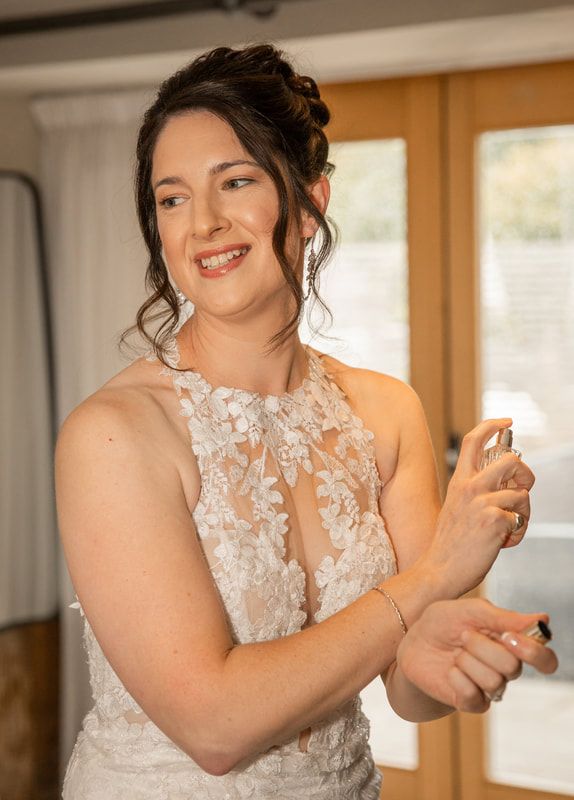 A person in a white lace wedding dress adjusts their jewelry while getting ready for their special day.