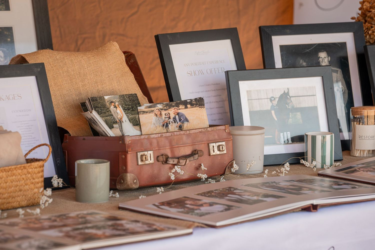 Vintage wedding memory table with framed photos, antique suitcase, mugs, and floral accents displayed at a reception.