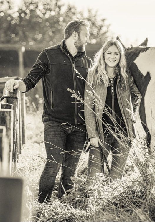 A couple sits together in tall grass during a romantic black and white outdoor photo session.