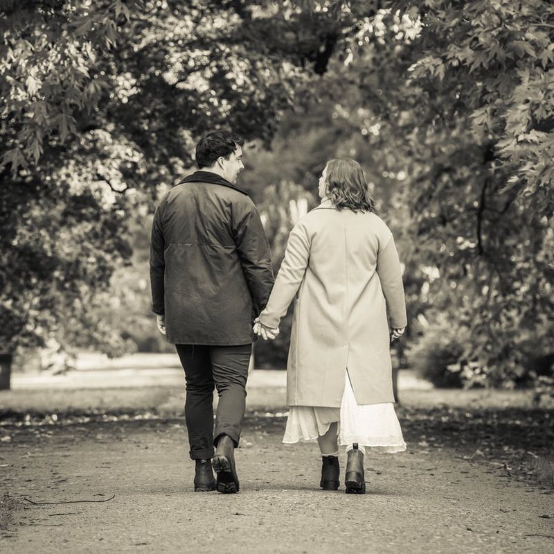 Two people walking away together on a path through a garden, captured in black and white photography.