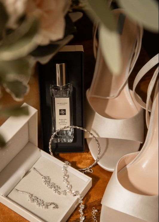 Elegant bridal jewelry and perfume bottle displayed on white stands against a wooden surface in warm lighting.