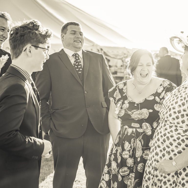 A candid black and white photo of guests laughing together during a festive outdoor celebration.