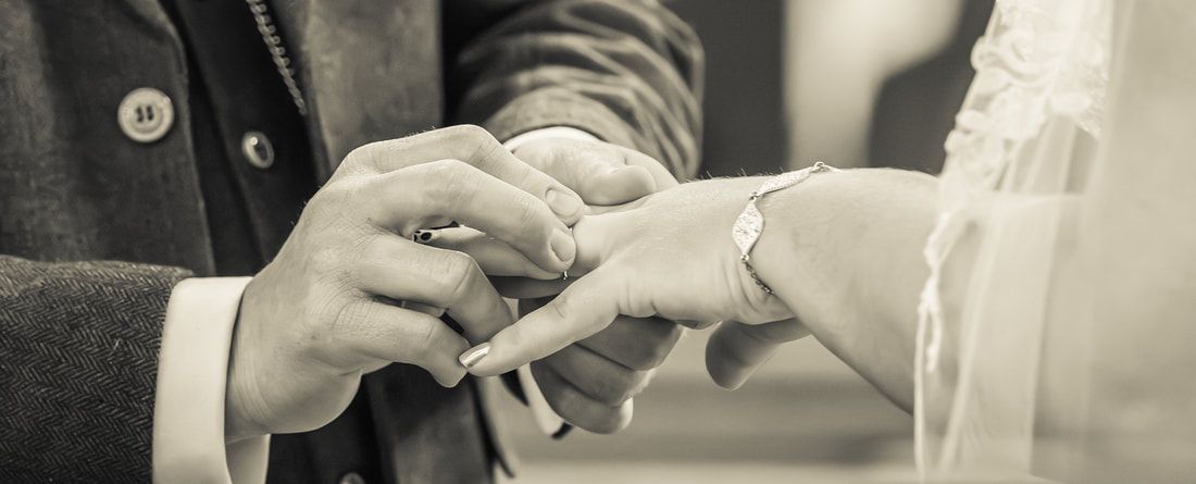 Black and white close-up of hands exchanging wedding rings during a marriage ceremony.