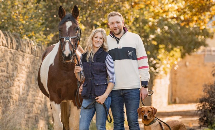 A couple poses with their brown horse and dog during an autumn engagement photoshoot outdoors.
