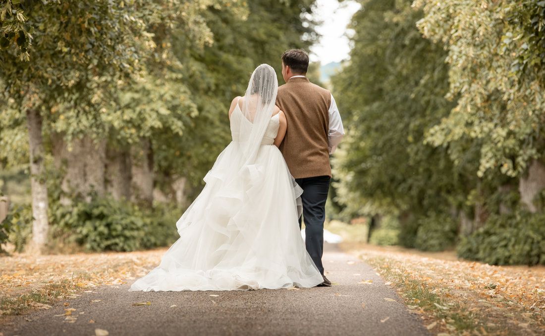 A couple in wedding attire walking down a tree-lined path together on their special day.