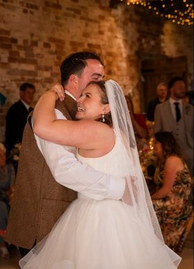 A couple shares a romantic first dance at their wedding reception in a rustic brick venue with twinkling lights.