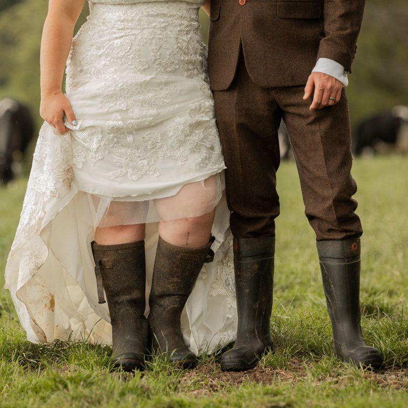 Couple wearing brown boots and white dress standing in green grass showing their country-style wedding footwear.