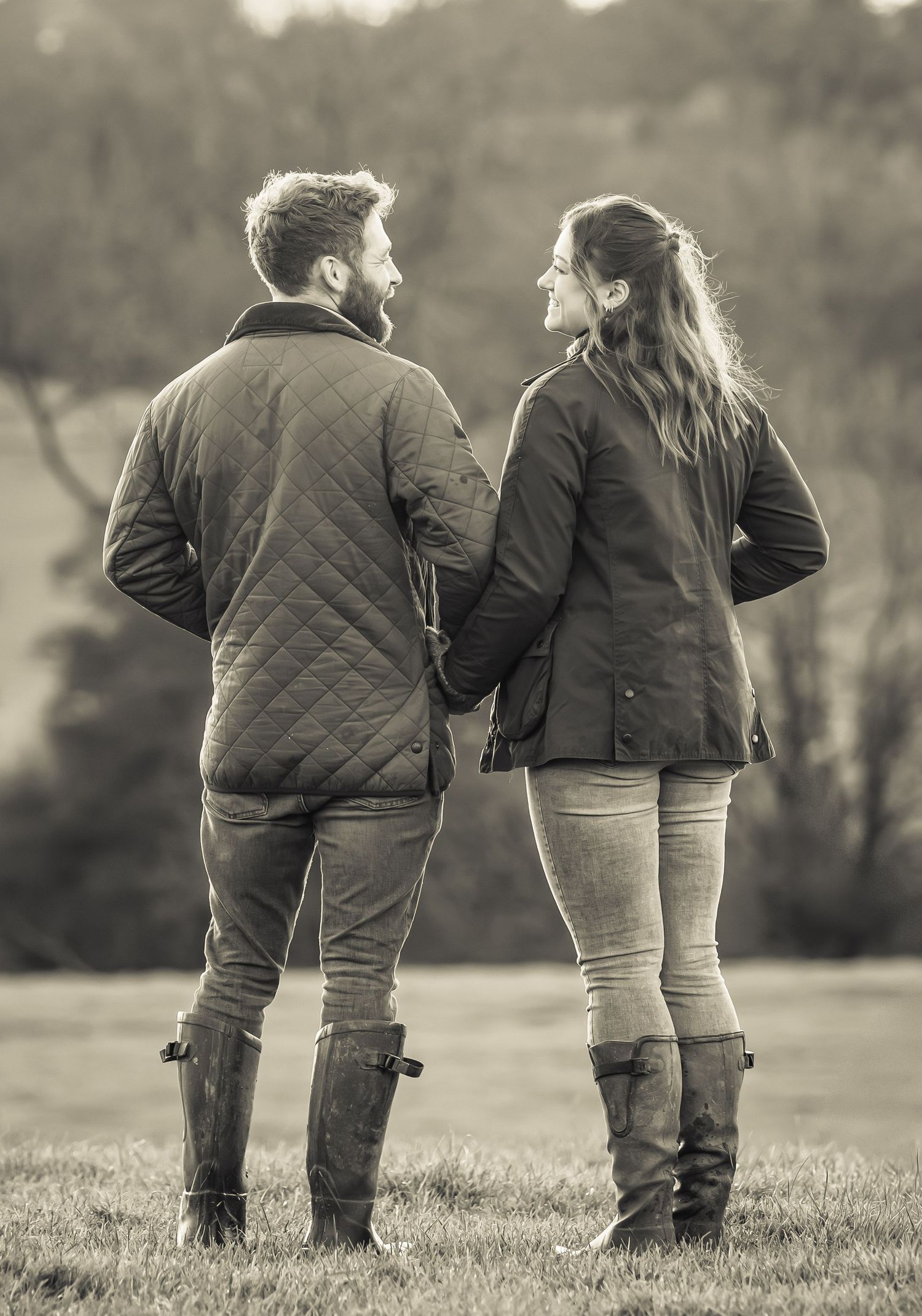 Black and white panoramic series shows two people in quilted jackets walking together across a grassy field.