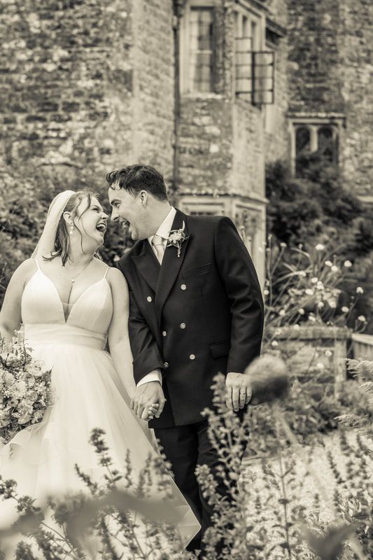 A romantic wedding couple shares a tender moment in a garden with stone walls and blooming flowers.
