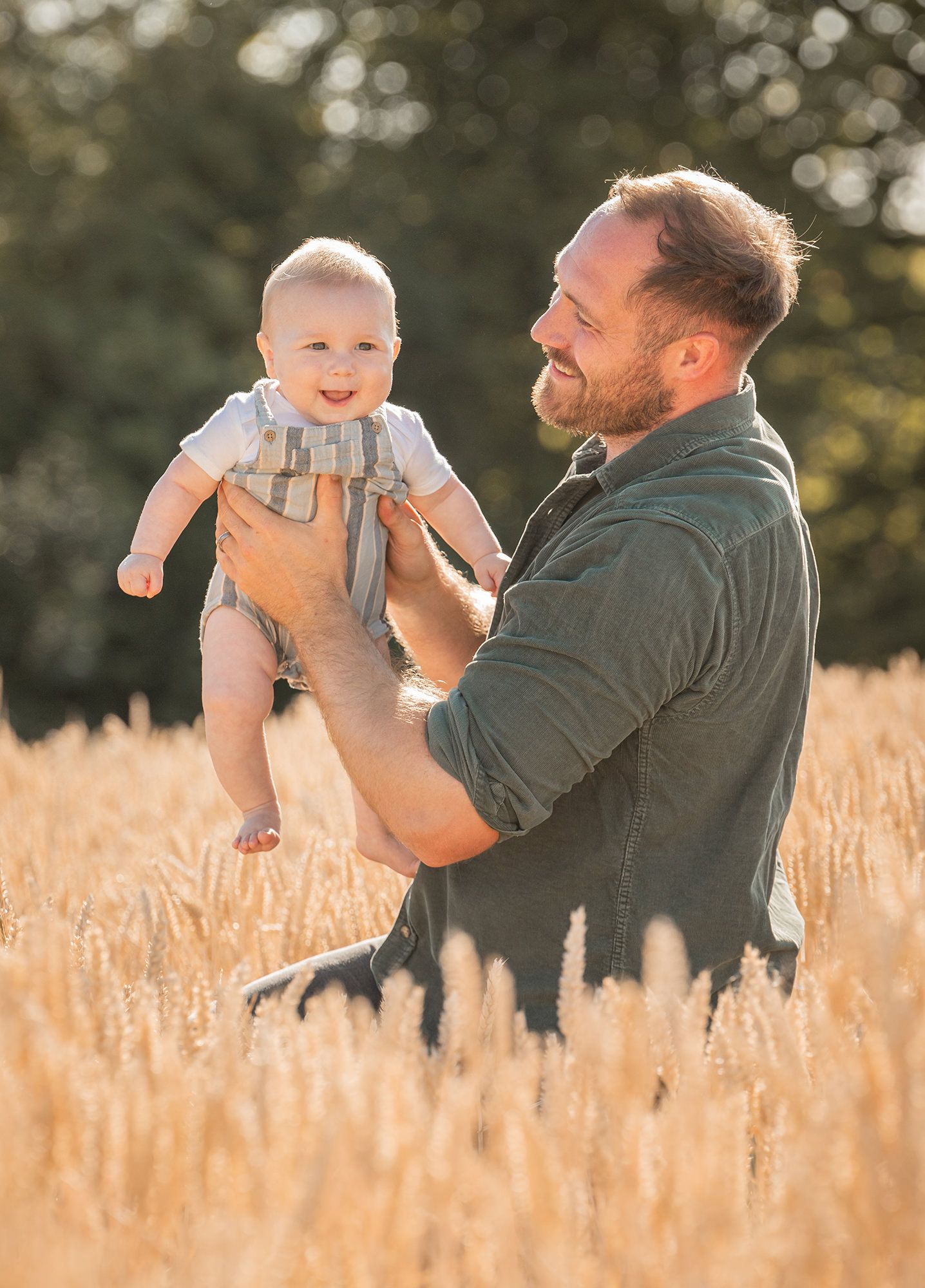 Farmer and his son sharing tender moments while sitting in tall golden wheat field on their family farm in the Cotswolds.