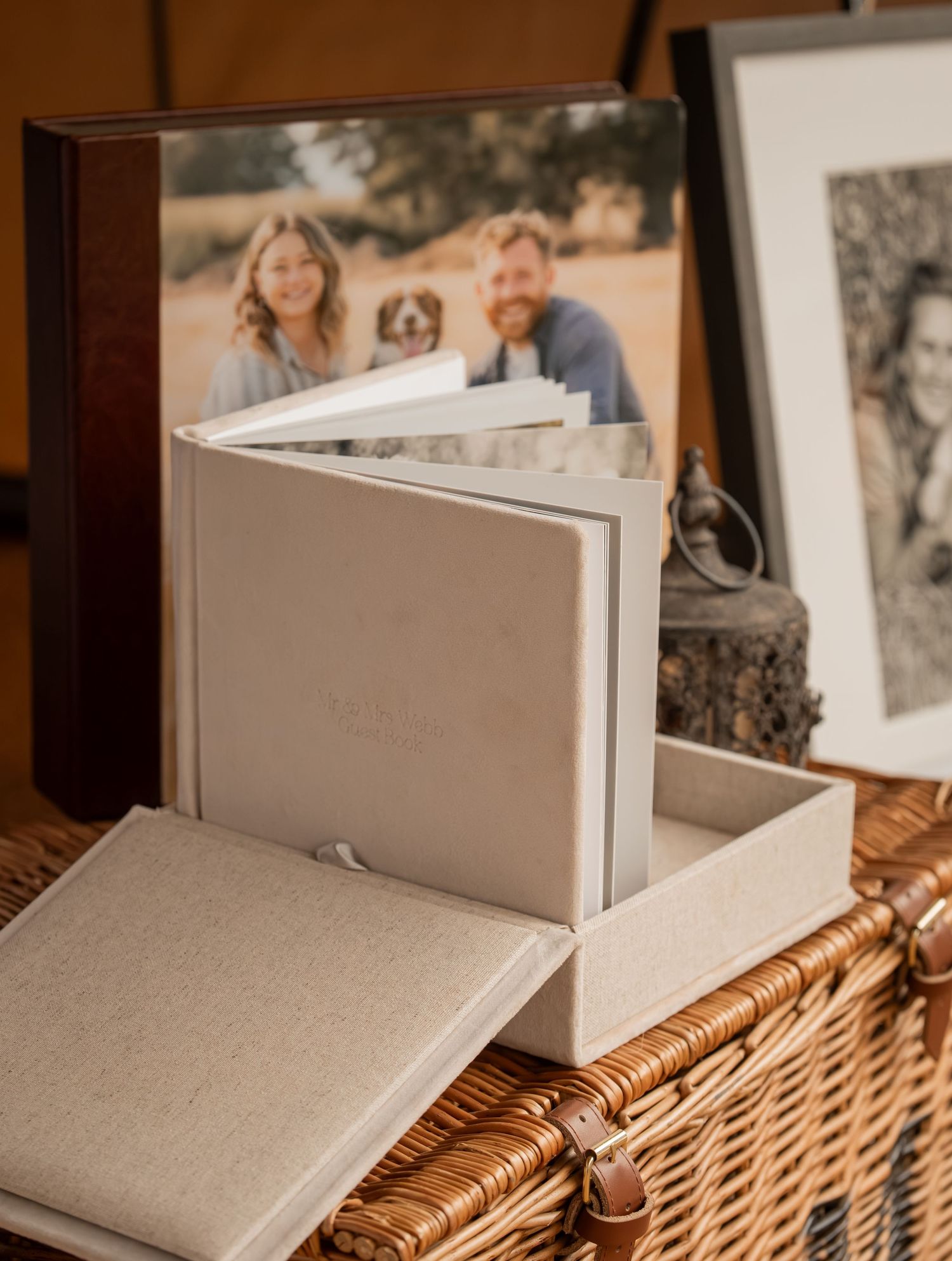 Elegant linen photo album in a keepsake box displayed on a wicker basket beside a framed couple portrait.