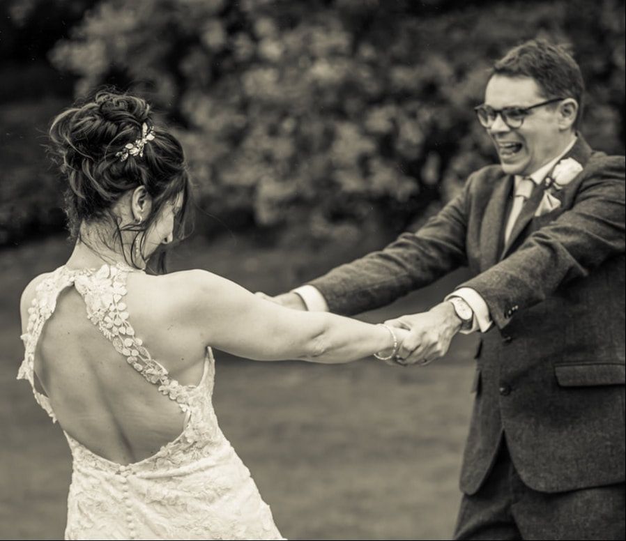 A black and white sequence of a bride and groom dancing together in a garden setting.
