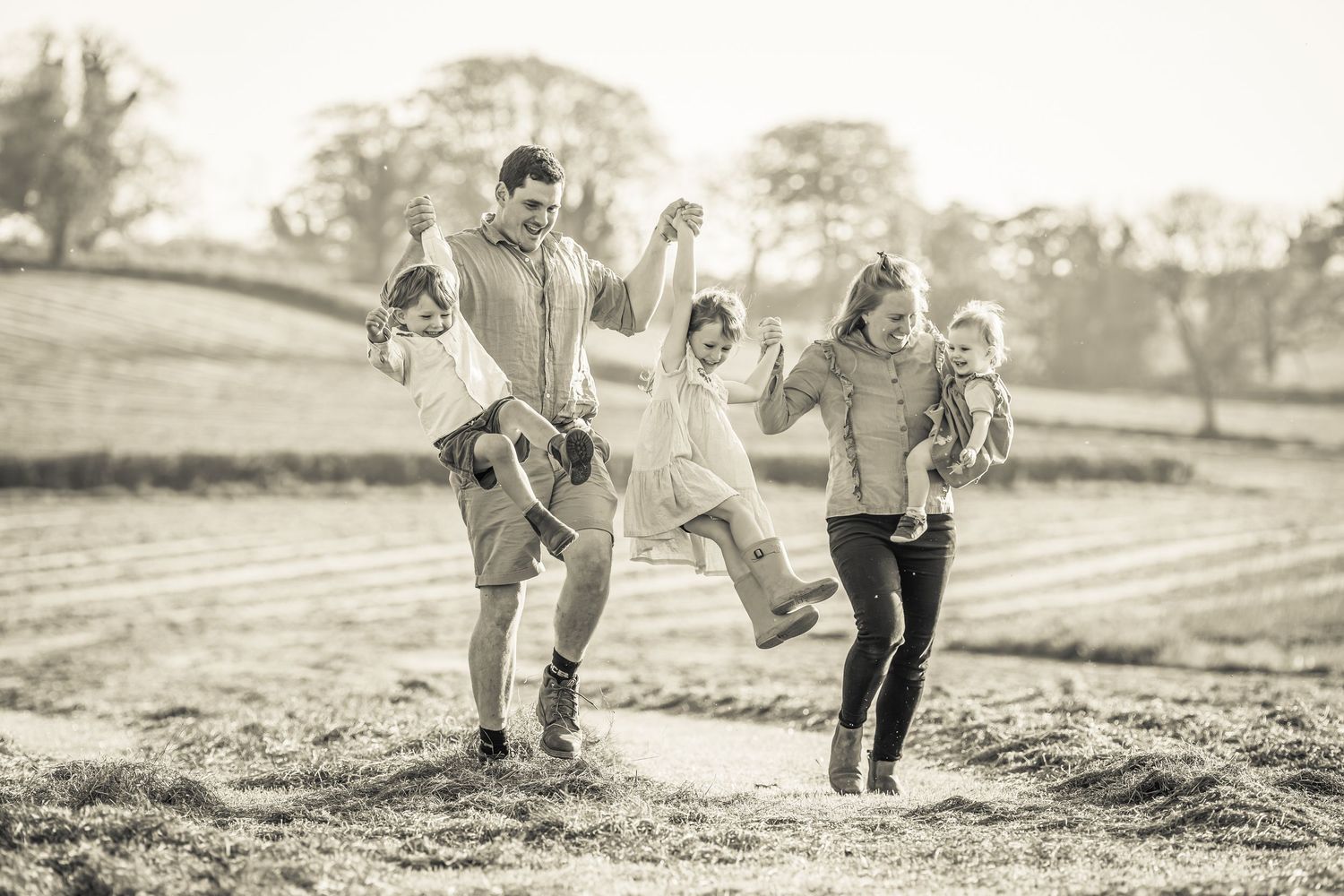A playful family photo session in black and white showing joyful moments in a field on their family farm near Shepton Mallet.