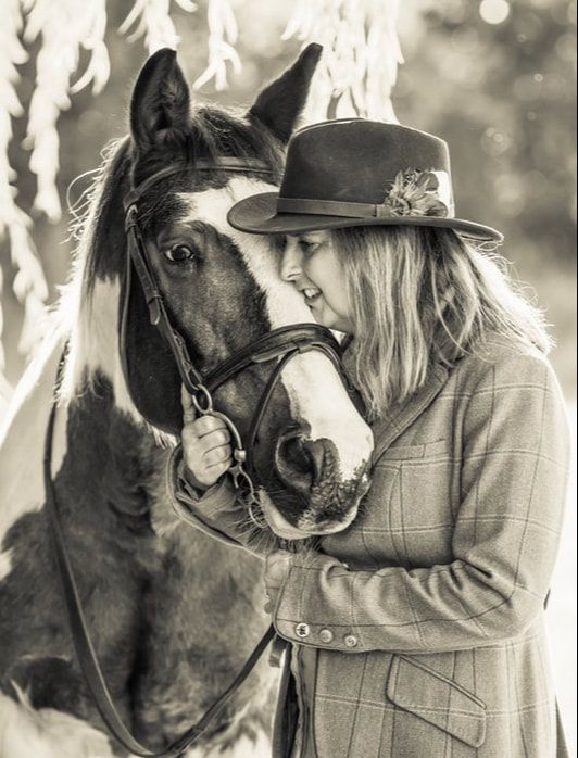 A black horse and person in western attire share an intimate bonding moment in a black and white photograph.