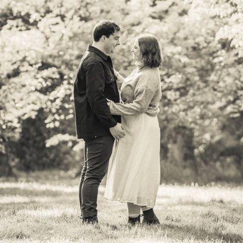 A romantic couple embraces in a sunlit meadow during a black and white engagement photo session.