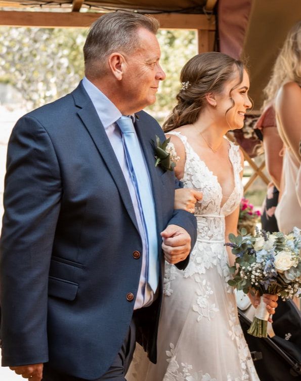 A wedding party laughs together during an outdoor celebration with natural lighting and floral bouquets.