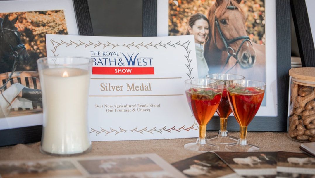 A silver medal certificate from Paths West displayed with two small glasses of red wine and a white candle.