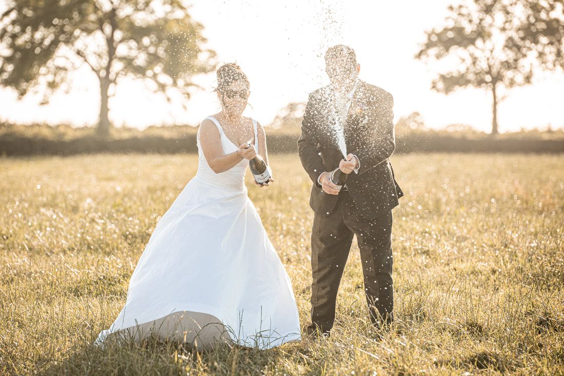 A couple in wedding attire walking through a sun-drenched field at golden hour creating a romantic silhouette.