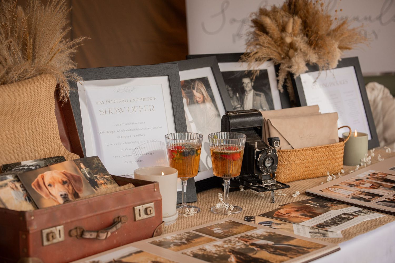 Vintage wedding memory table with antique camera, amber drinks, old photographs, framed portraits, and pampas grass decor.
