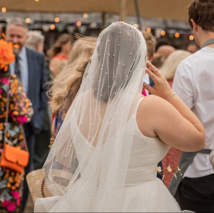 A bride in a flowing white wedding dress and veil dances with guests during a wedding reception celebration.