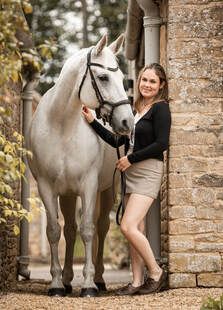 A white horse stands near a brick wall while someone pets its neck during an outdoor photo session.