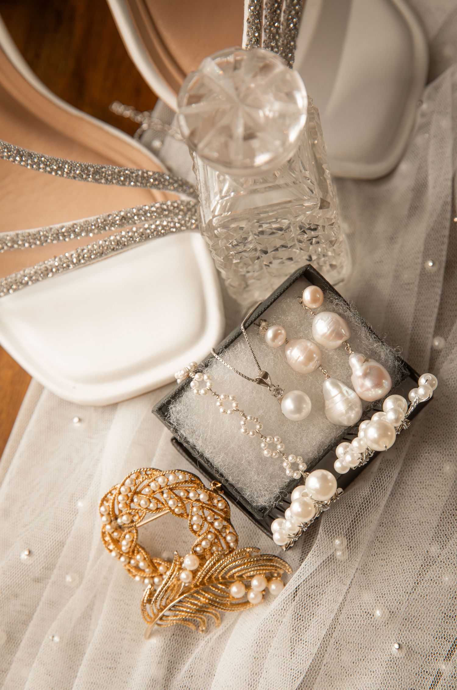 Elegant wedding accessories including pearl jewelry and rhinestone details on white fabric.