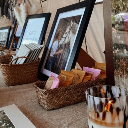 Framed photographs displayed in woven baskets on a table with a glass of iced coffee in the foreground.