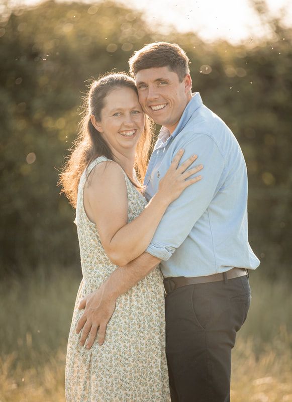 Romantic couple embraces in a sunlit field during golden hour creating a dreamy outdoor portrait series.