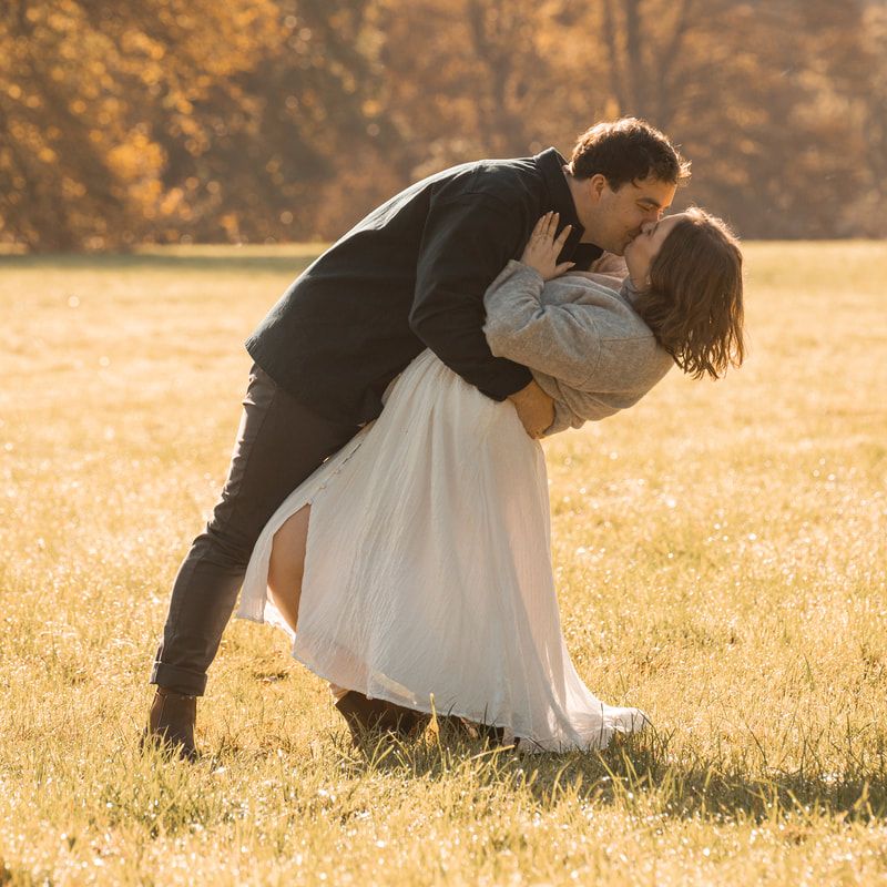 Couple in formal attire embraces on a golden sunlit meadow during sunset in autumn.