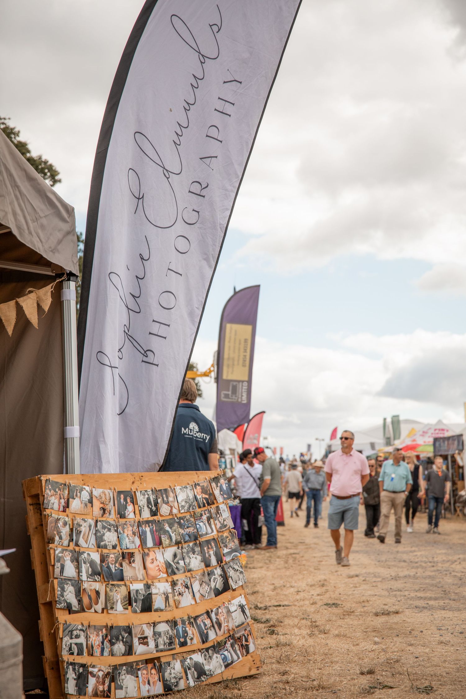 Sophie Edwards Photography booth at outdoor festival with banner, photo display board, and crowd in background.