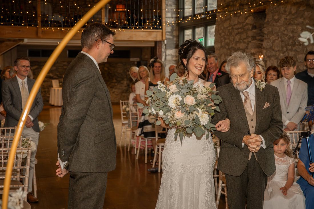 Guests celebrate and dance during an evening wedding reception in a rustic barn venue with string lights overhead.
