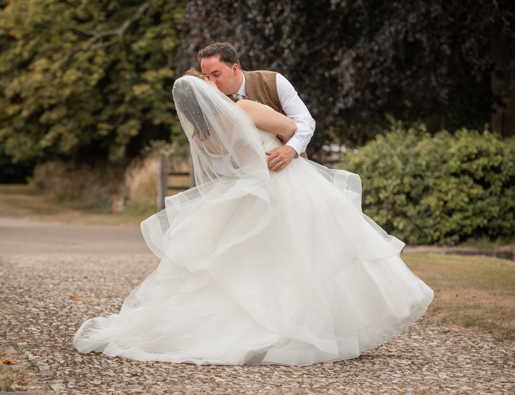 A romantic wedding couple embraces on a gravel path surrounded by lush greenery in an outdoor garden setting.