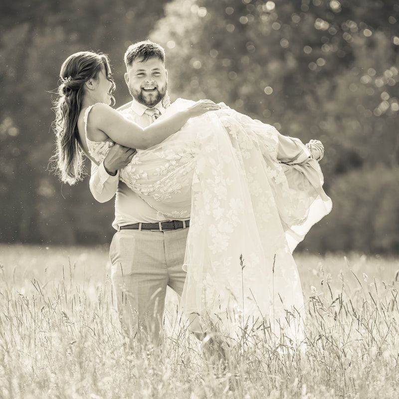 A romantic couple dances and twirls together in a sunlit meadow wearing wedding attire in black and white.