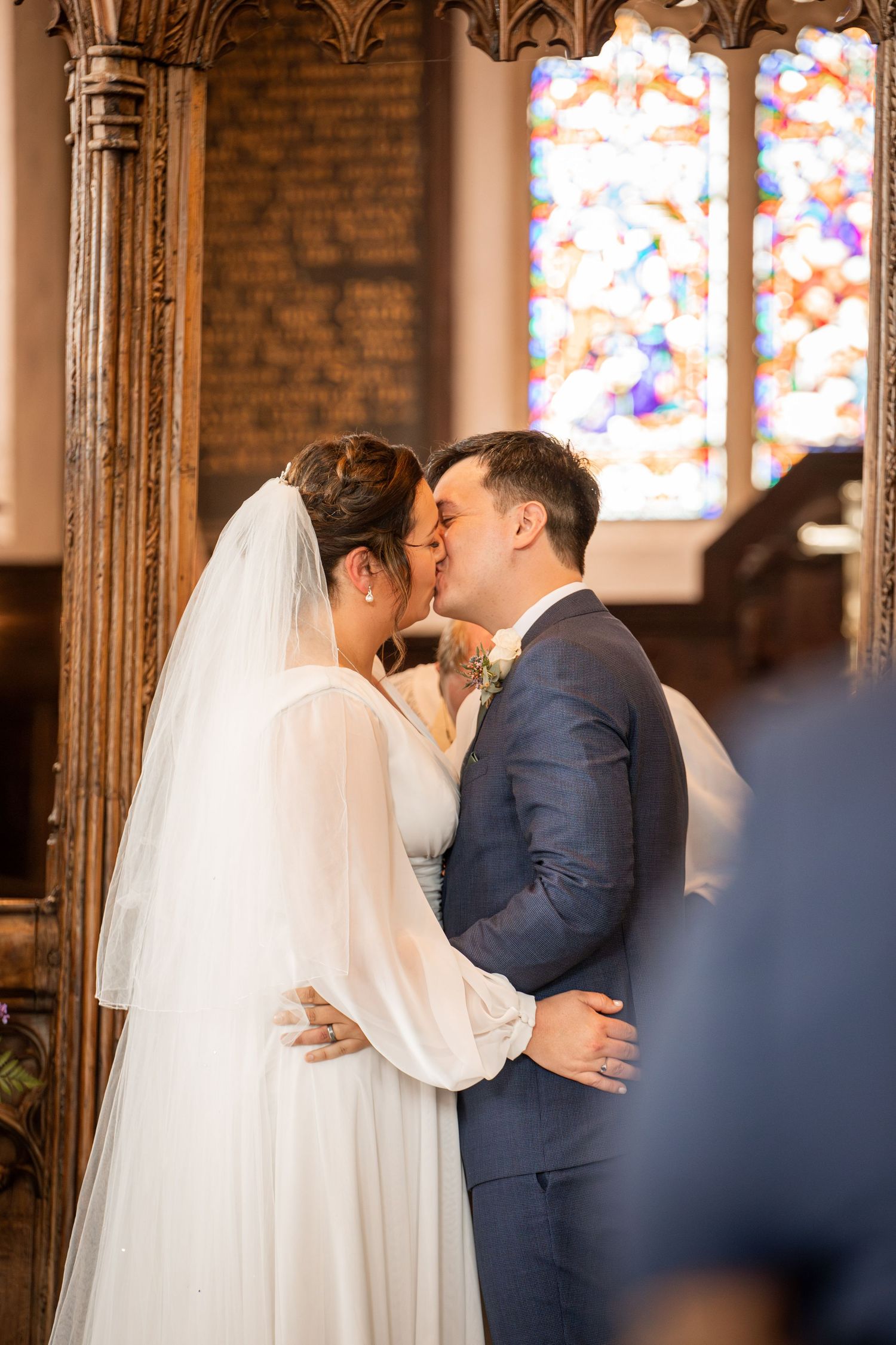 A sequence of romantic first kiss moments between newlyweds in a church with brick walls and stained glass windows.