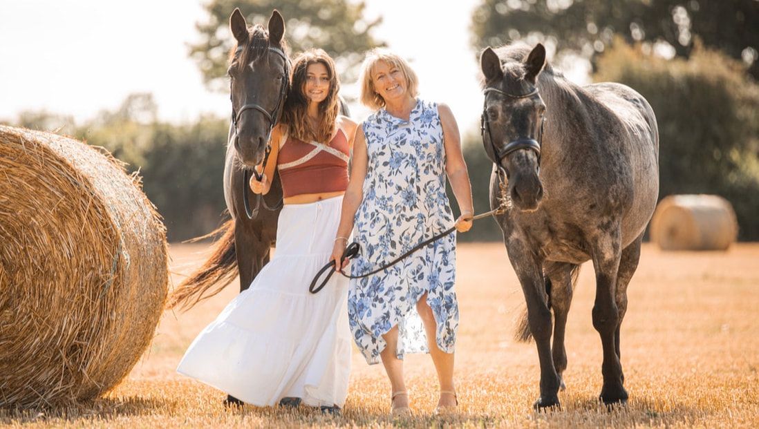 Two people walk together on a dirt path with a horse during a golden sunset in a rural setting.