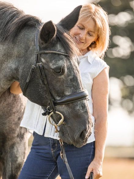 A person in a white top shares a tender moment with a black horse against a soft bokeh background.