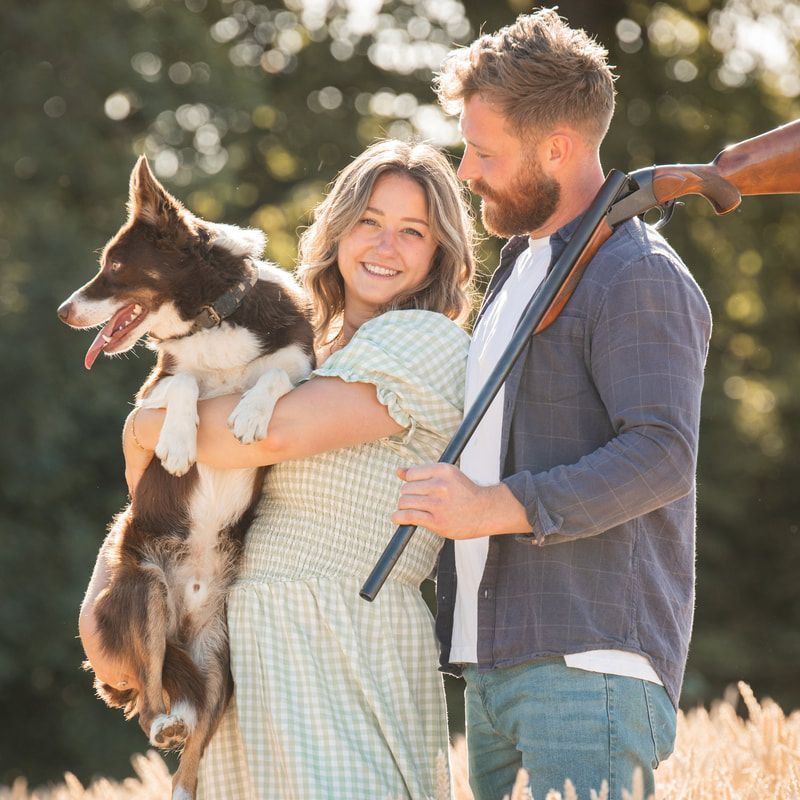 A couple holding their Border Collie dog outdoors in warm sunlight during a casual photo session.
