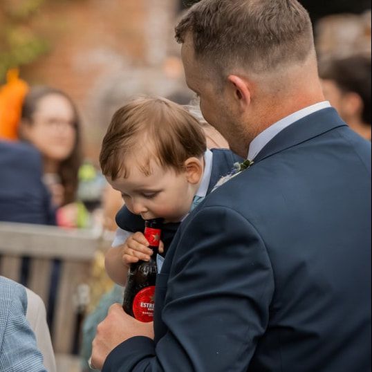 A young boy in a suit holds a red ring pop candy while standing among a crowd at a formal event.