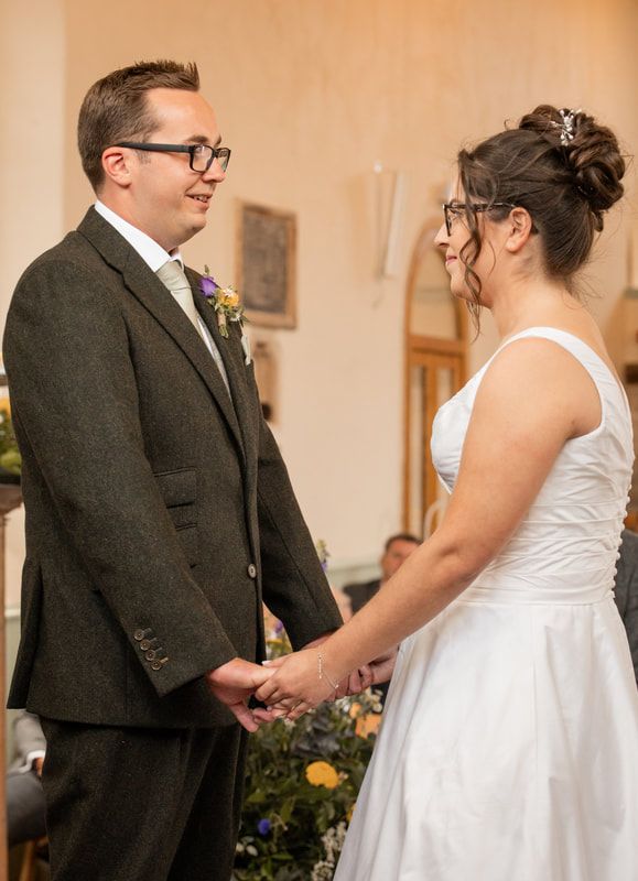 A couple holds hands during their wedding ceremony in a church with warm lighting and floral decorations.