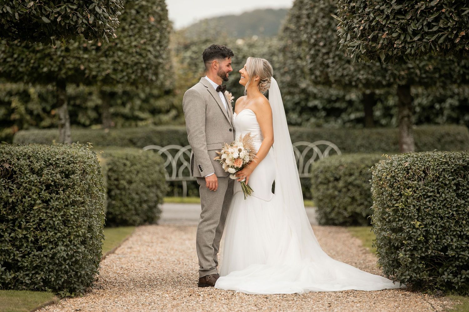 Wedding couple poses in formal garden setting in Devon with manicured hedges whilst being photographed by Sophie Edmunds Photography