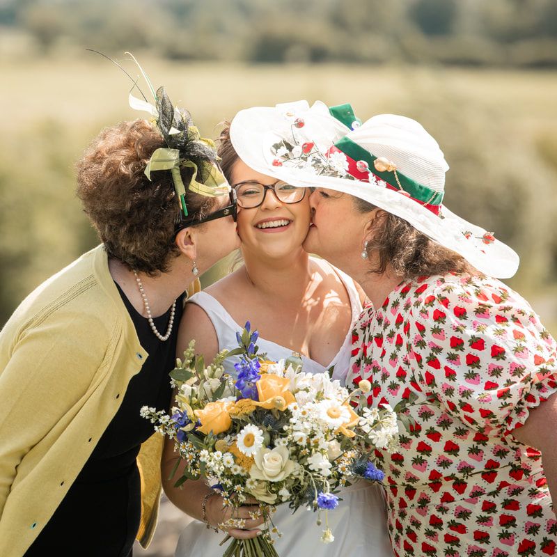 Three people share a joyful moment outdoors with a beautiful bouquet of wildflowers and white and yellow blooms.