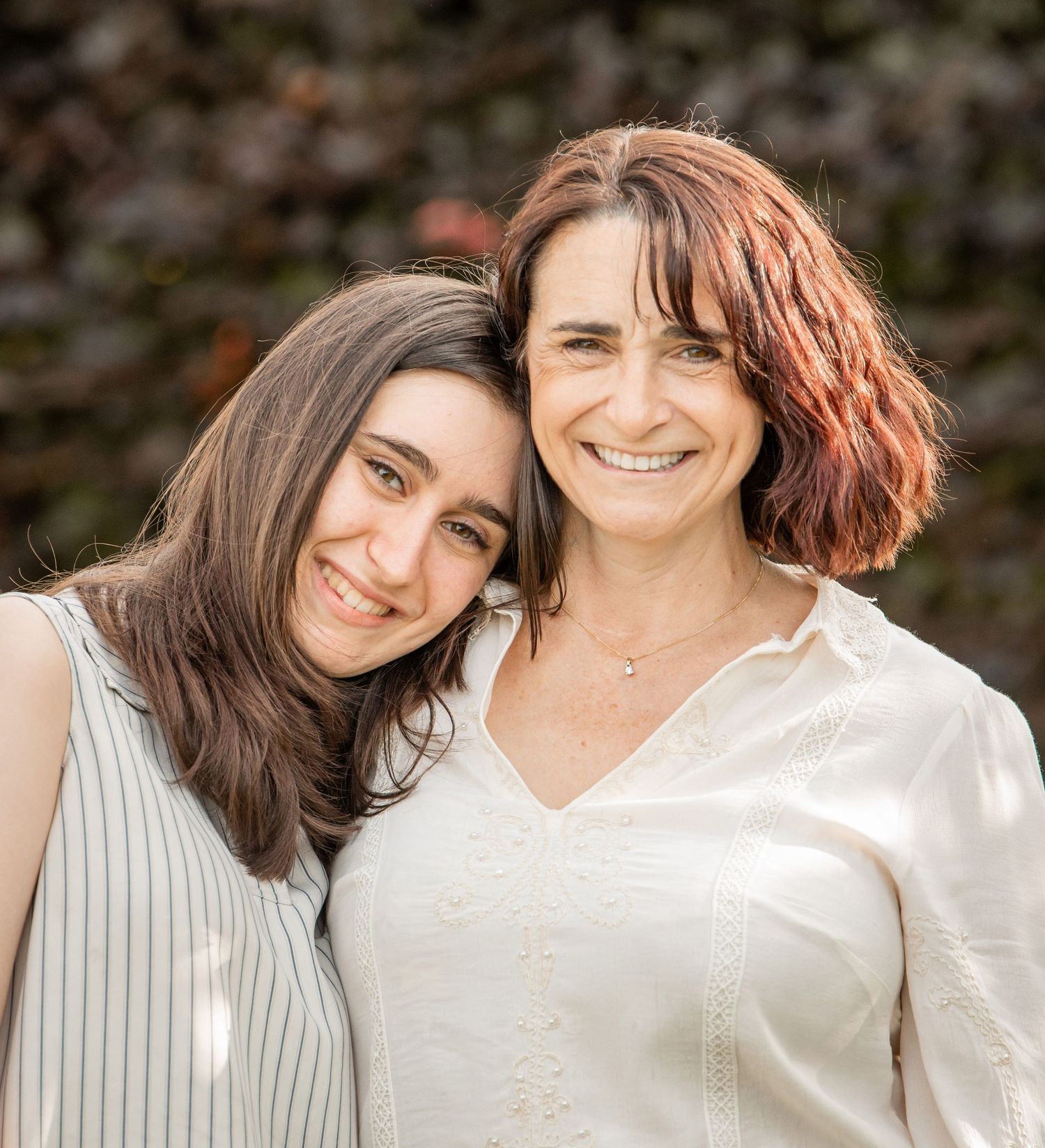 Two people in white tops share a joyful moment together outdoors with natural lighting and bokeh background.