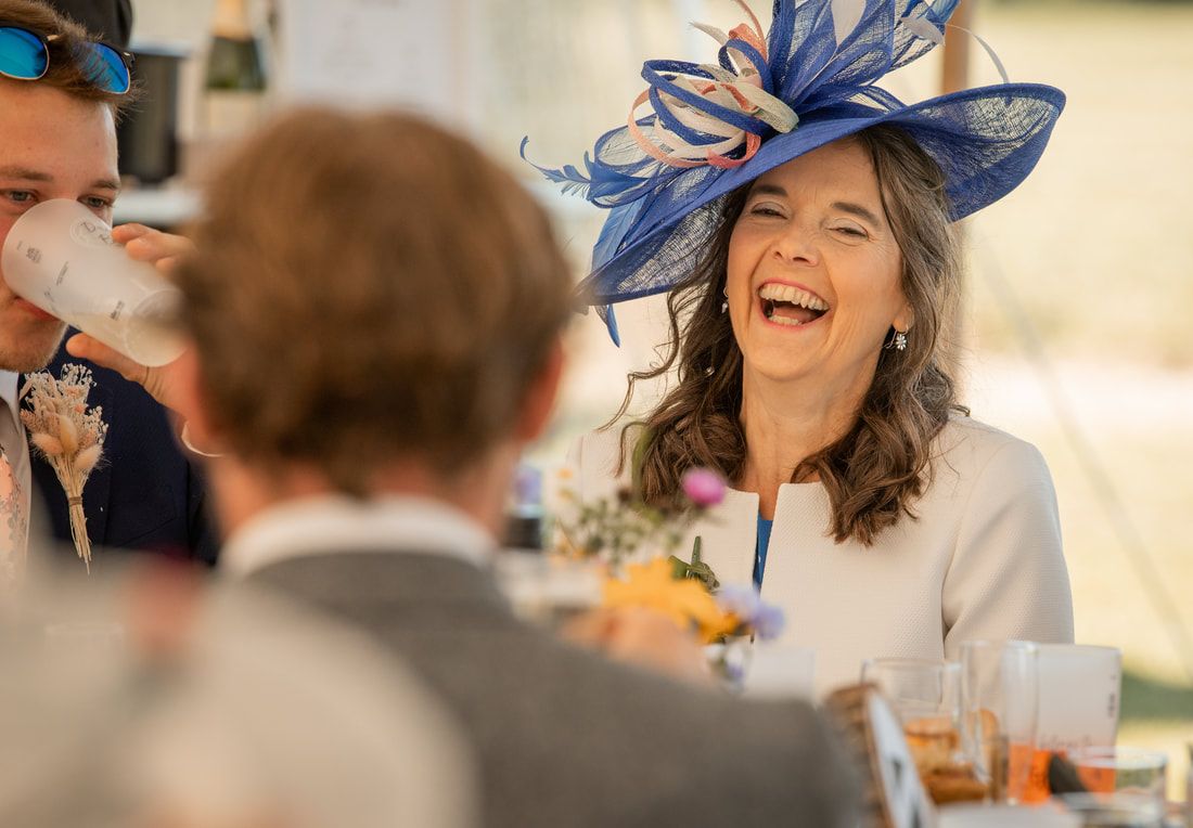 Group of people wearing elegant blue fascinators and hats while laughing and enjoying themselves at a formal event.