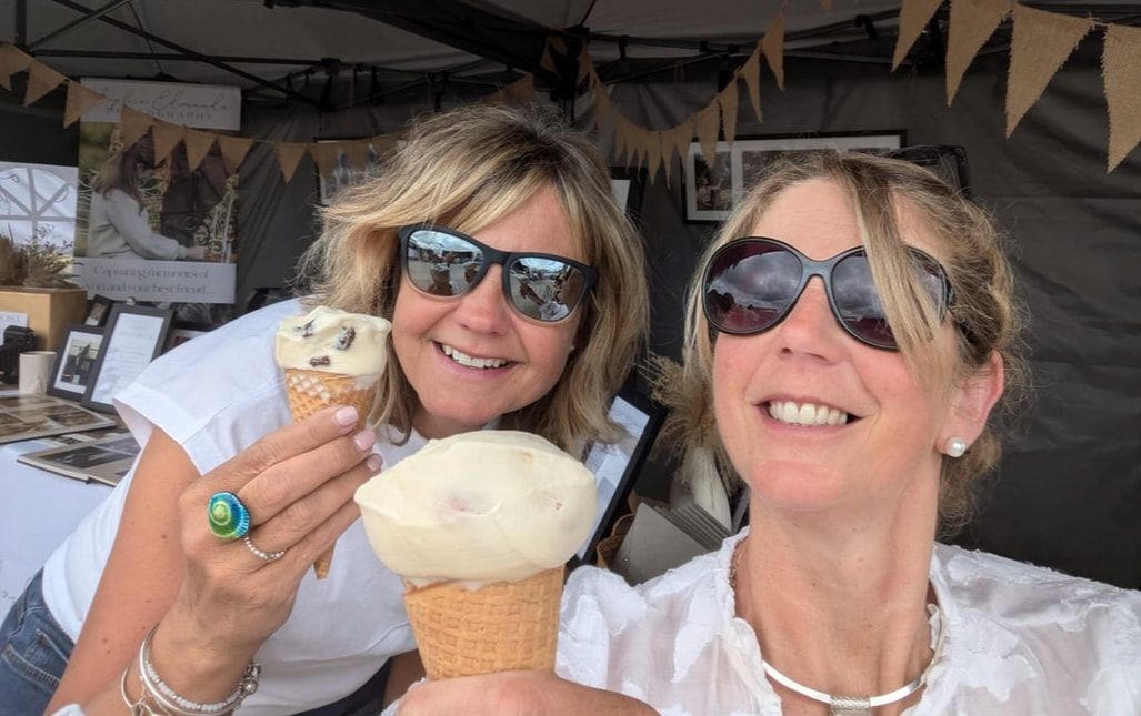 A group of friends wearing sunglasses smile while enjoying cupcakes together at an outdoor gathering.