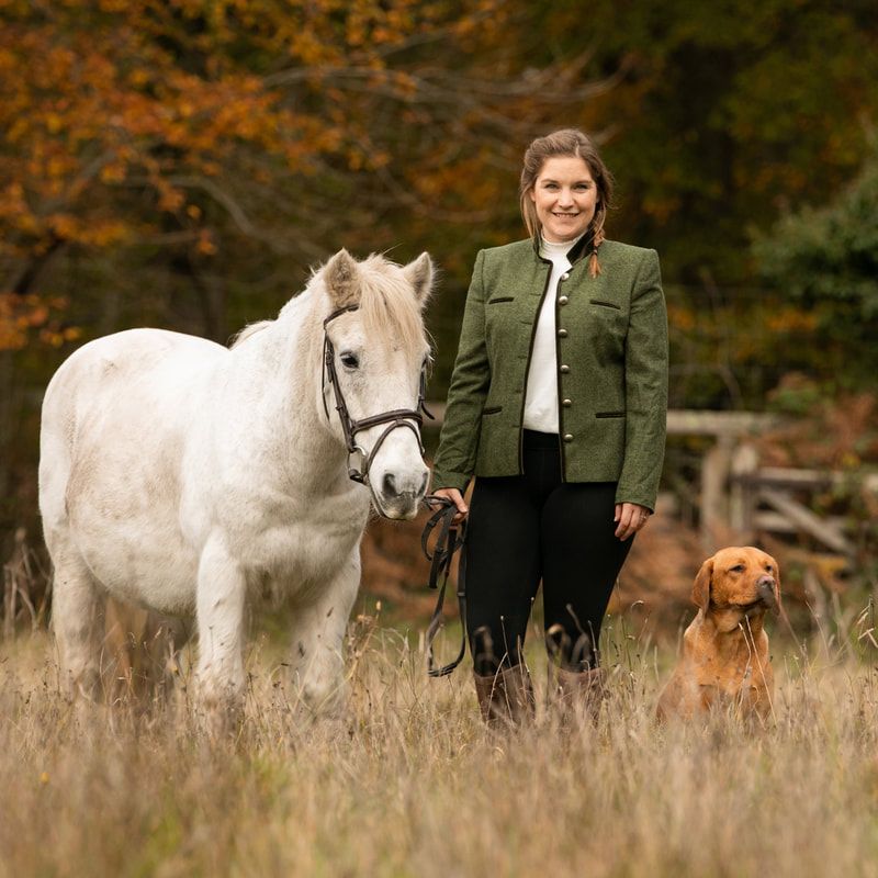 White horses and dogs walking through tall autumn grass with handlers.