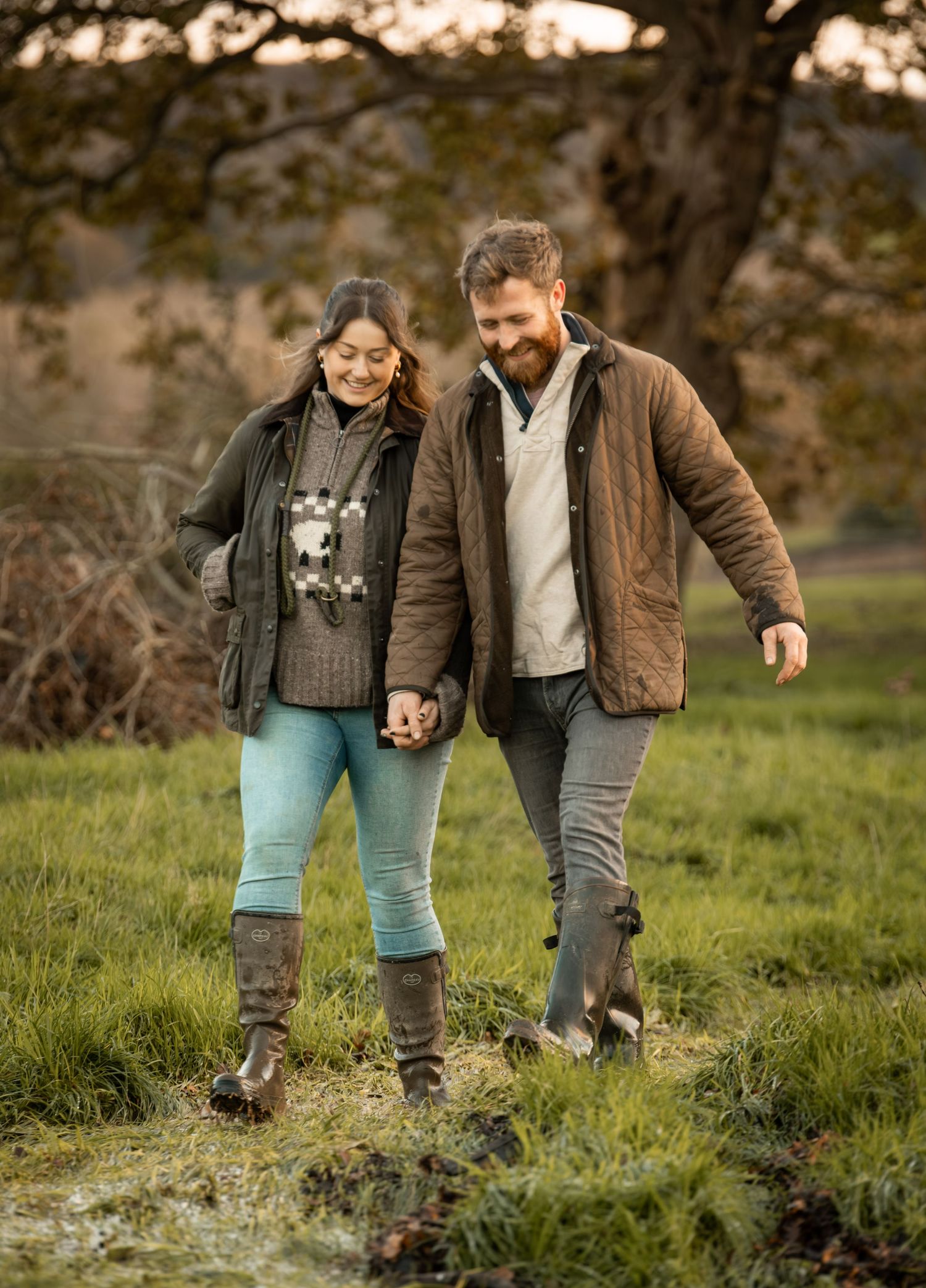 A couple walking together on a grassy path during golden hour, holding hands in a romantic outdoor setting.